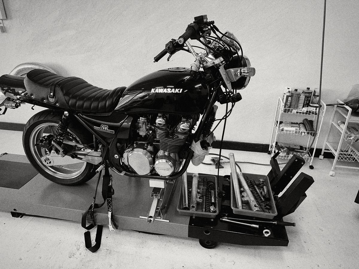 リフトに載せて整備中のバイクと、外したフロントフォークの部品